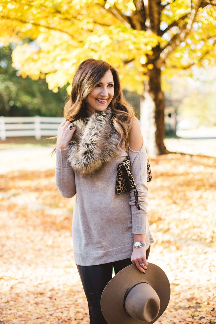 Blogger Mallory Fitzsimmons of Style Your Senses wears a cold shoulder tunic sweater with faux leather leggings, a faux fur infinity scarf and felt hat for a festive Fall and Winter look. 